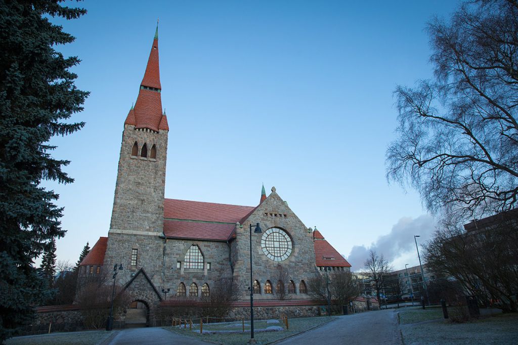 Tampereen tuomiokirkko marraskuisen sunnuntain hämärässä päivässä. Puut ovat paljaita ja taivas tumma.