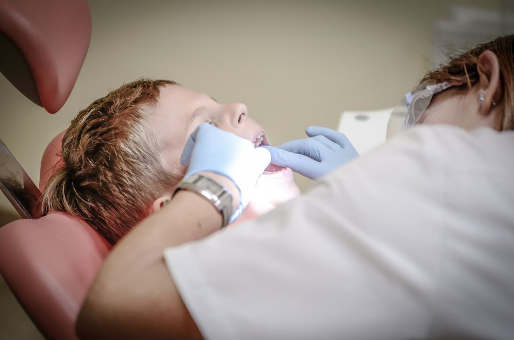 Hammaslääkäri tutkii lapsipotilaan hampaita kumartuneena tämän ylle.