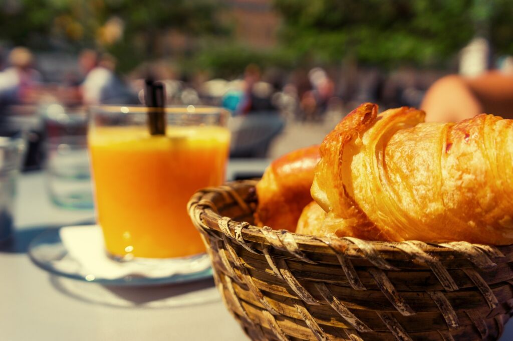 Lasillinen appelsiinimehua ja etualalla korissa croissantteja.